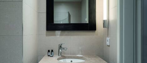 A bathroom with a sink, mirror, and two bottles on the counter.