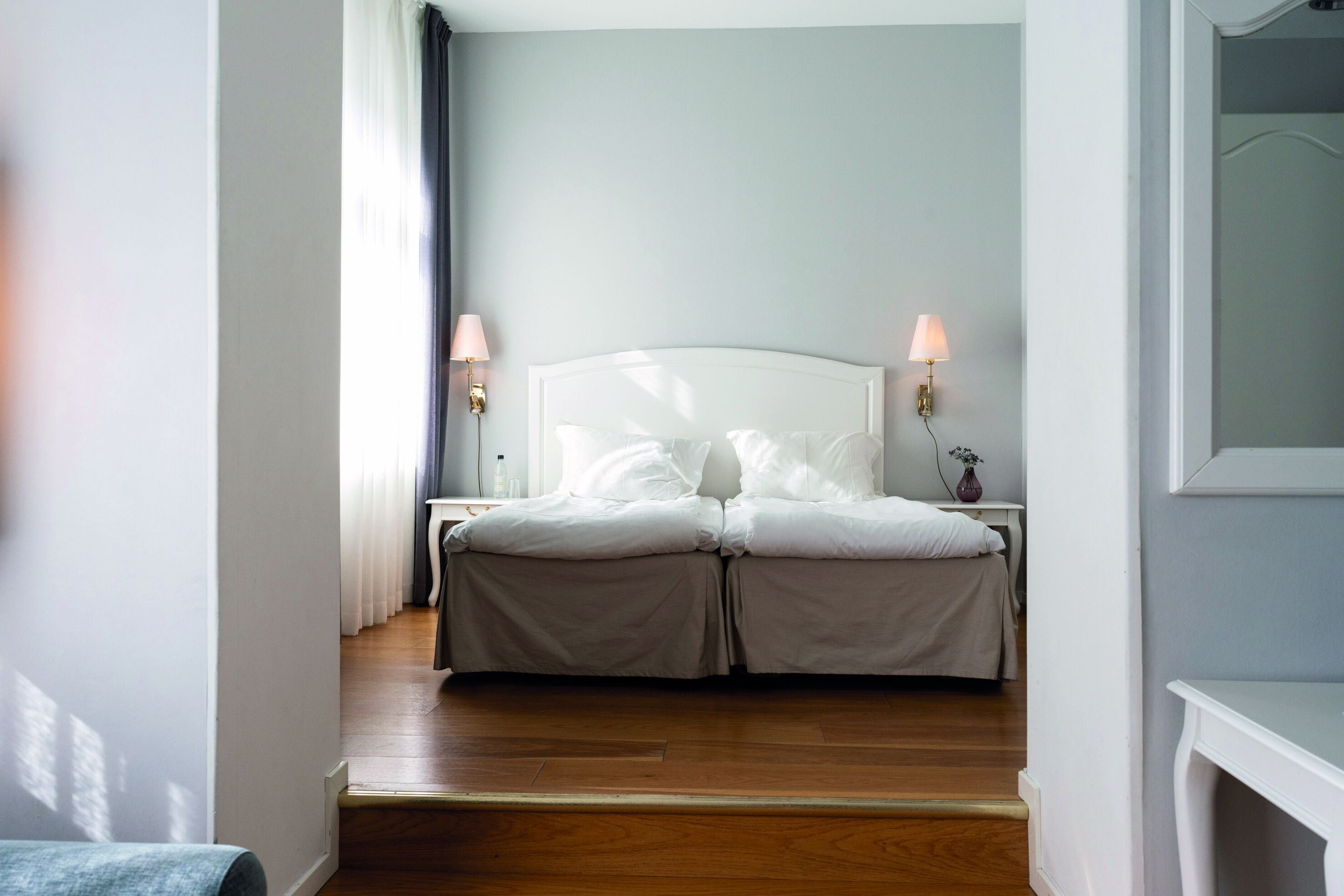 Ein Schlafzimmer mit einem weißen Bett, zwei Nachttischlampen und einem Holzboden.