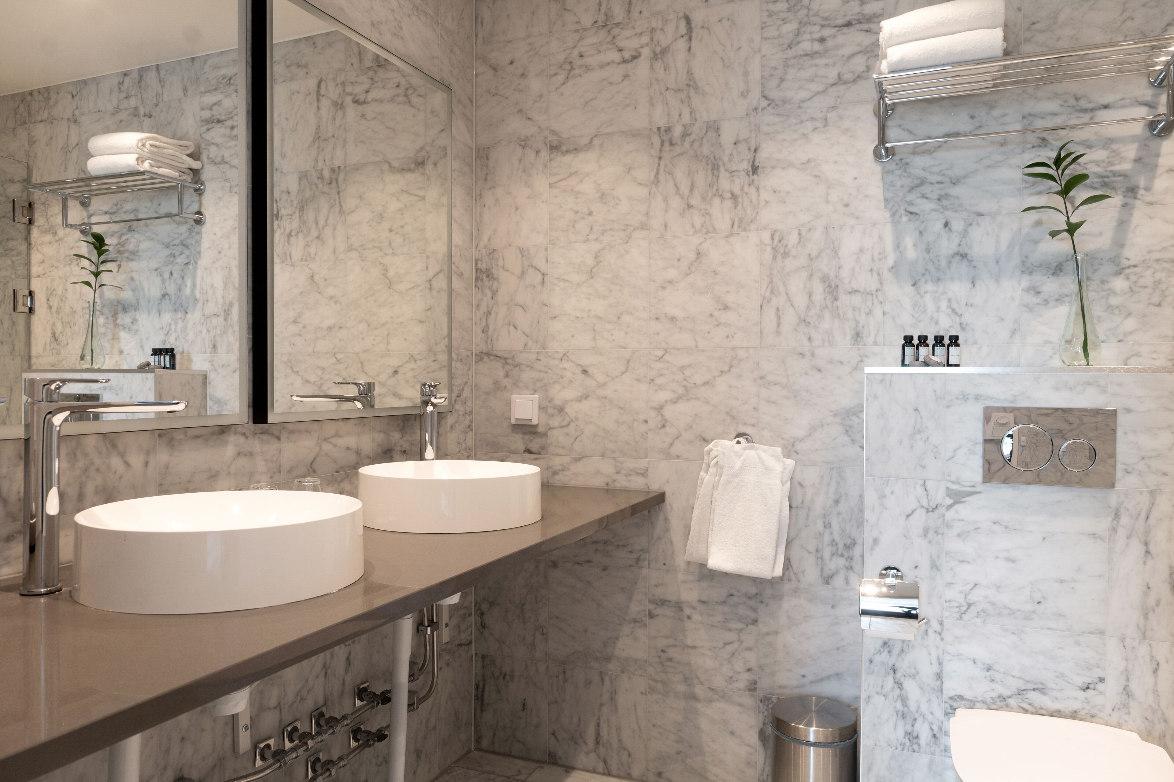A modern bathroom with two sinks, a large mirror, and marble walls.