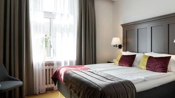 A hotel room with a bed, a chair, a nightstand, and a window with curtains.