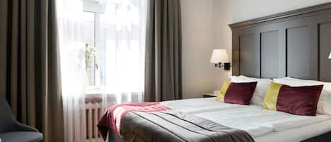 A hotel room with a bed, a chair, a nightstand, and a window with curtains.