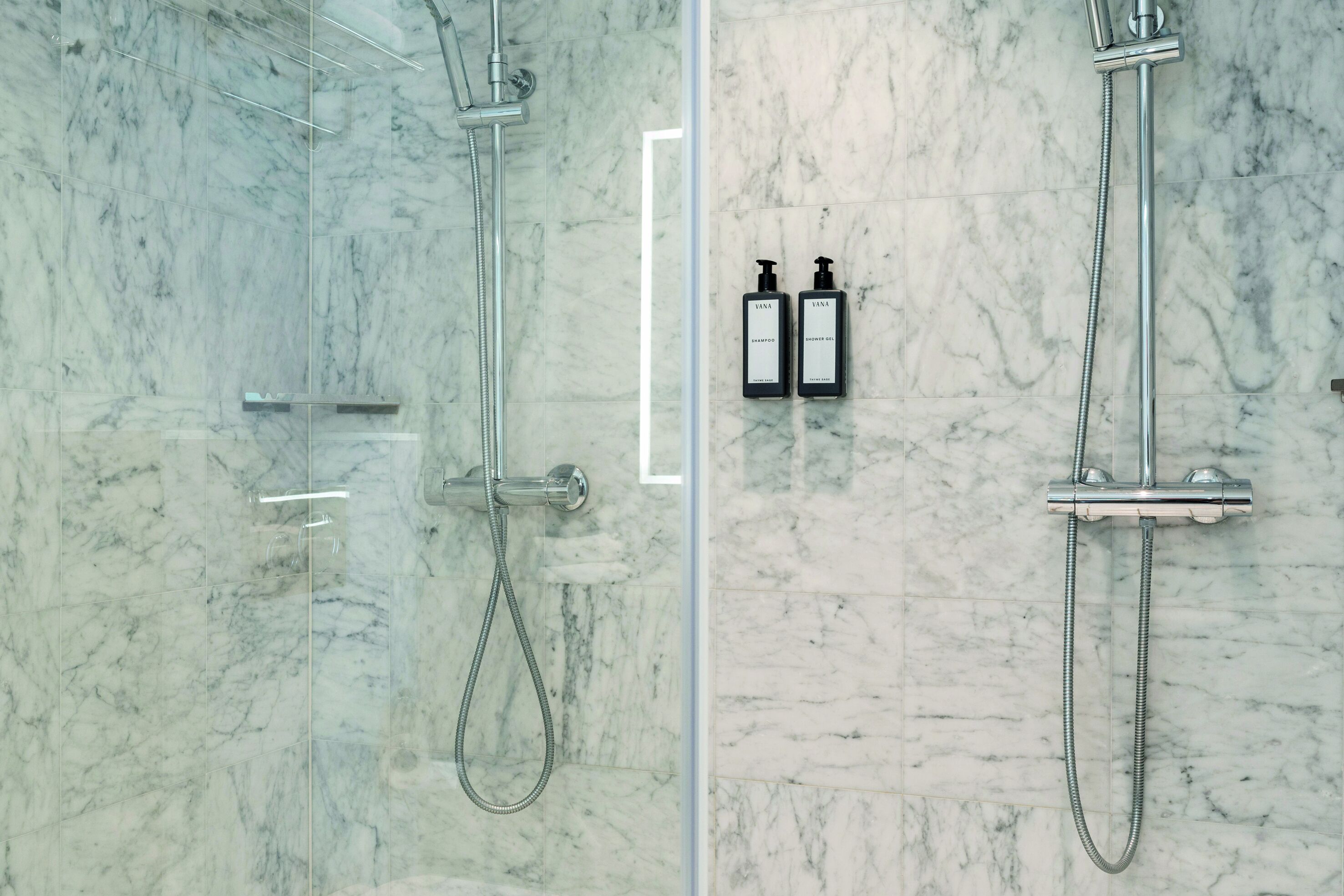 A bathroom with a glass-enclosed shower and a marble wall.