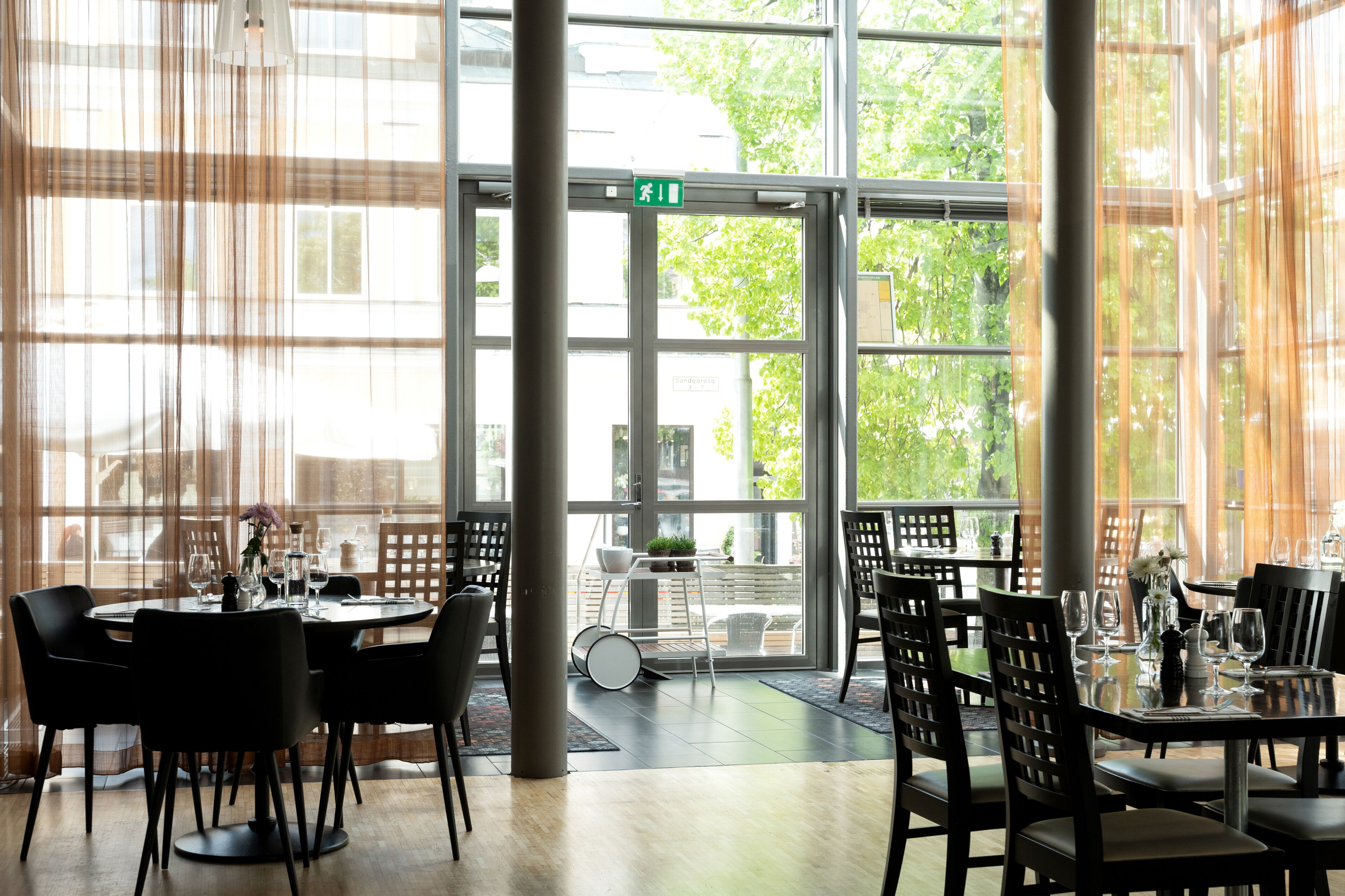 Un restaurante con ventanas amplias, mesas dispuestas con sillas y vistas al exterior.