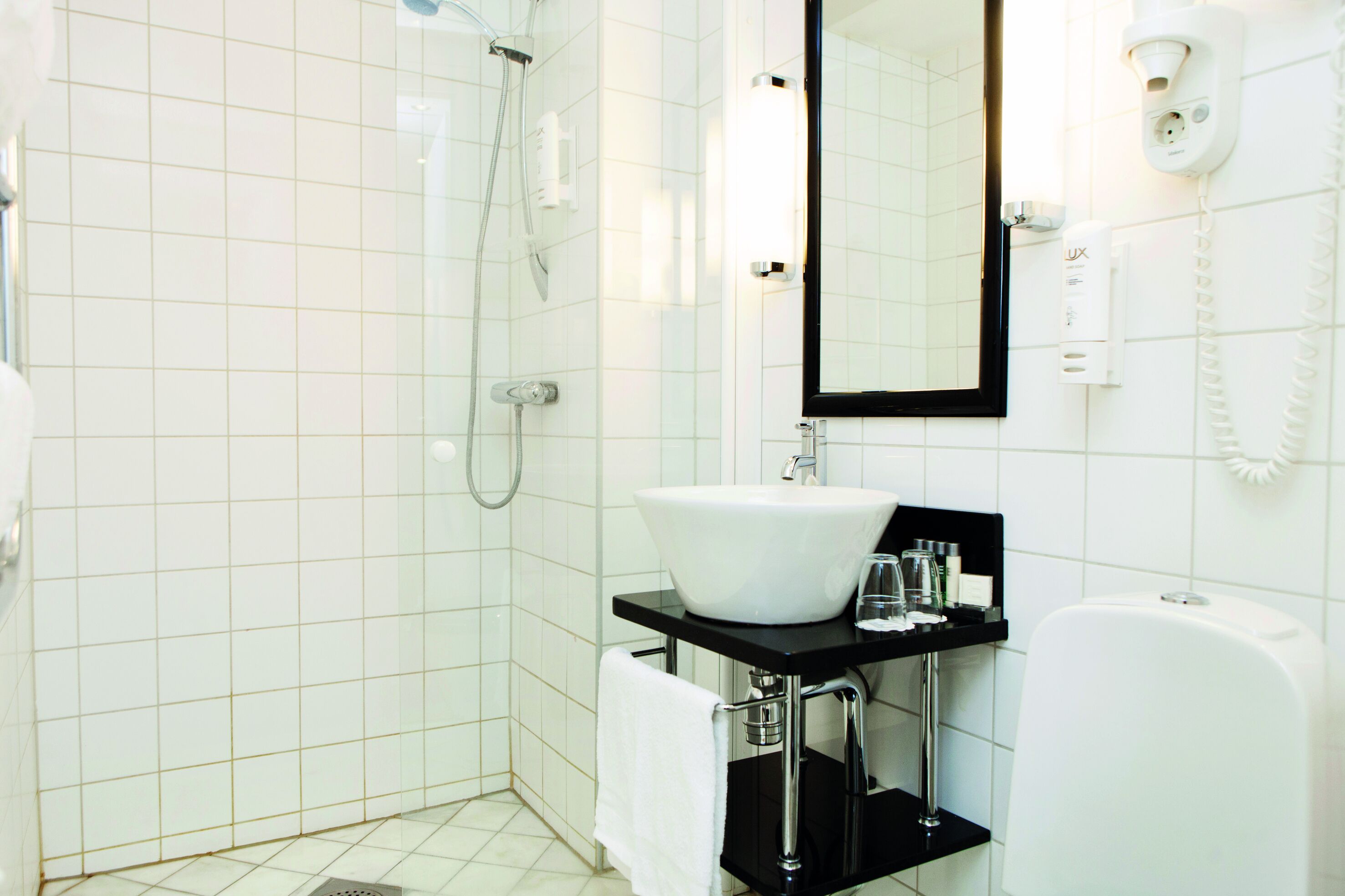 A modern bathroom with a white sink, black countertop, and a glass shower enclosure.