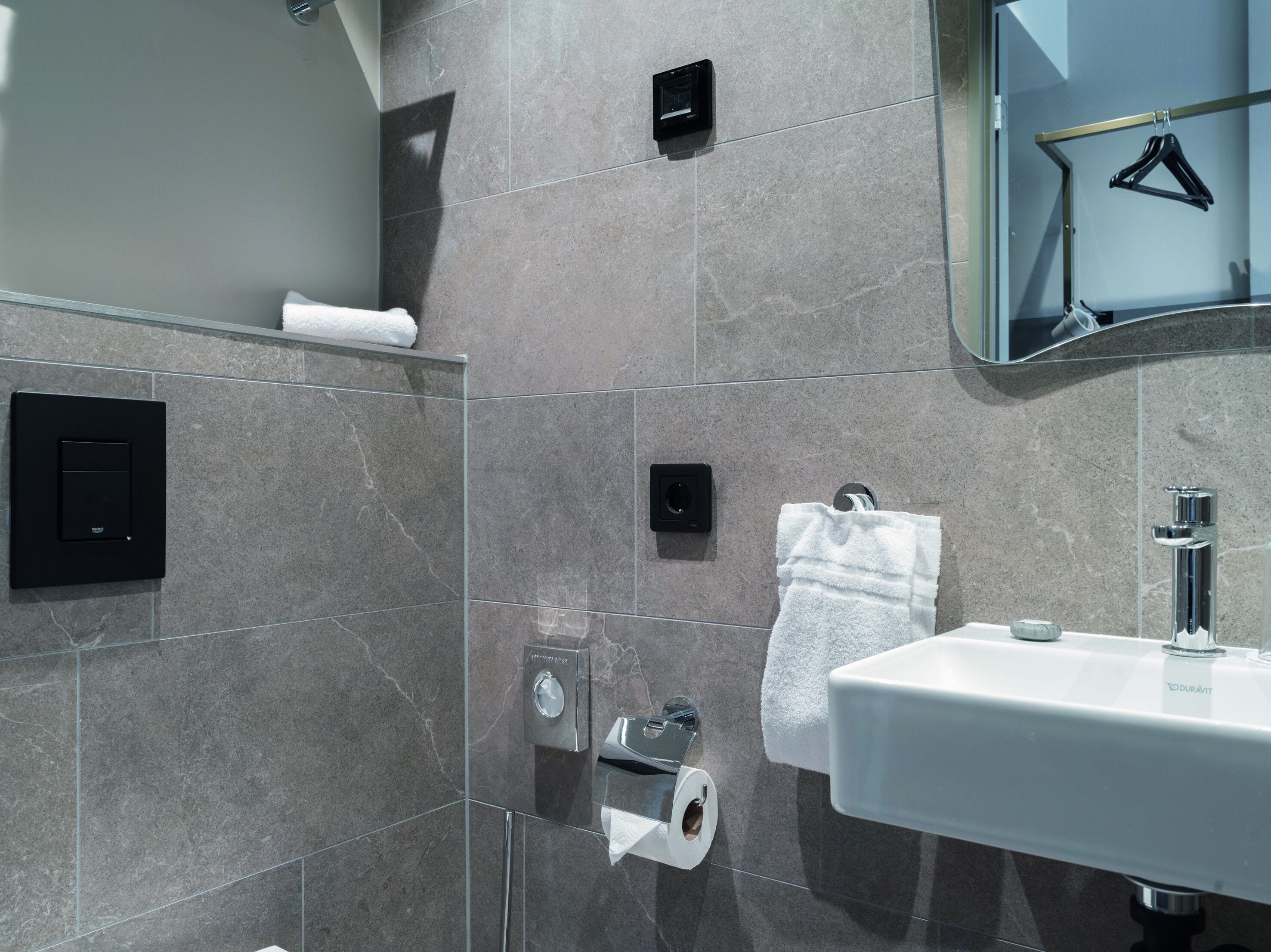 A modern bathroom with a glass shower enclosure, a white sink, and a towel rack.