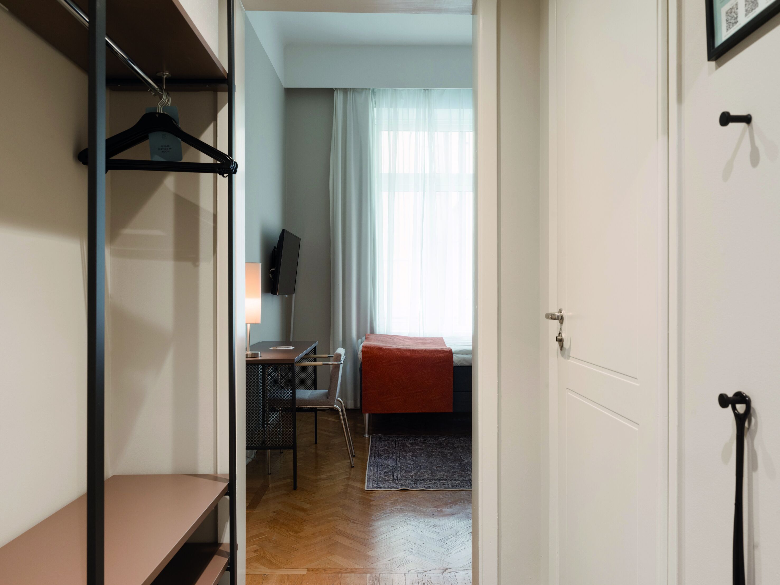 Una habitación de hotel con cama, escritorio, silla, televisor y armario.