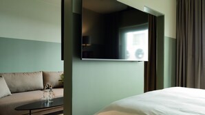 A modern hotel room with a large bed, a sofa, a coffee table with glasses, and a flat-screen TV mounted on the wall. - Elite Stadshotellet Växjö (Växjö)