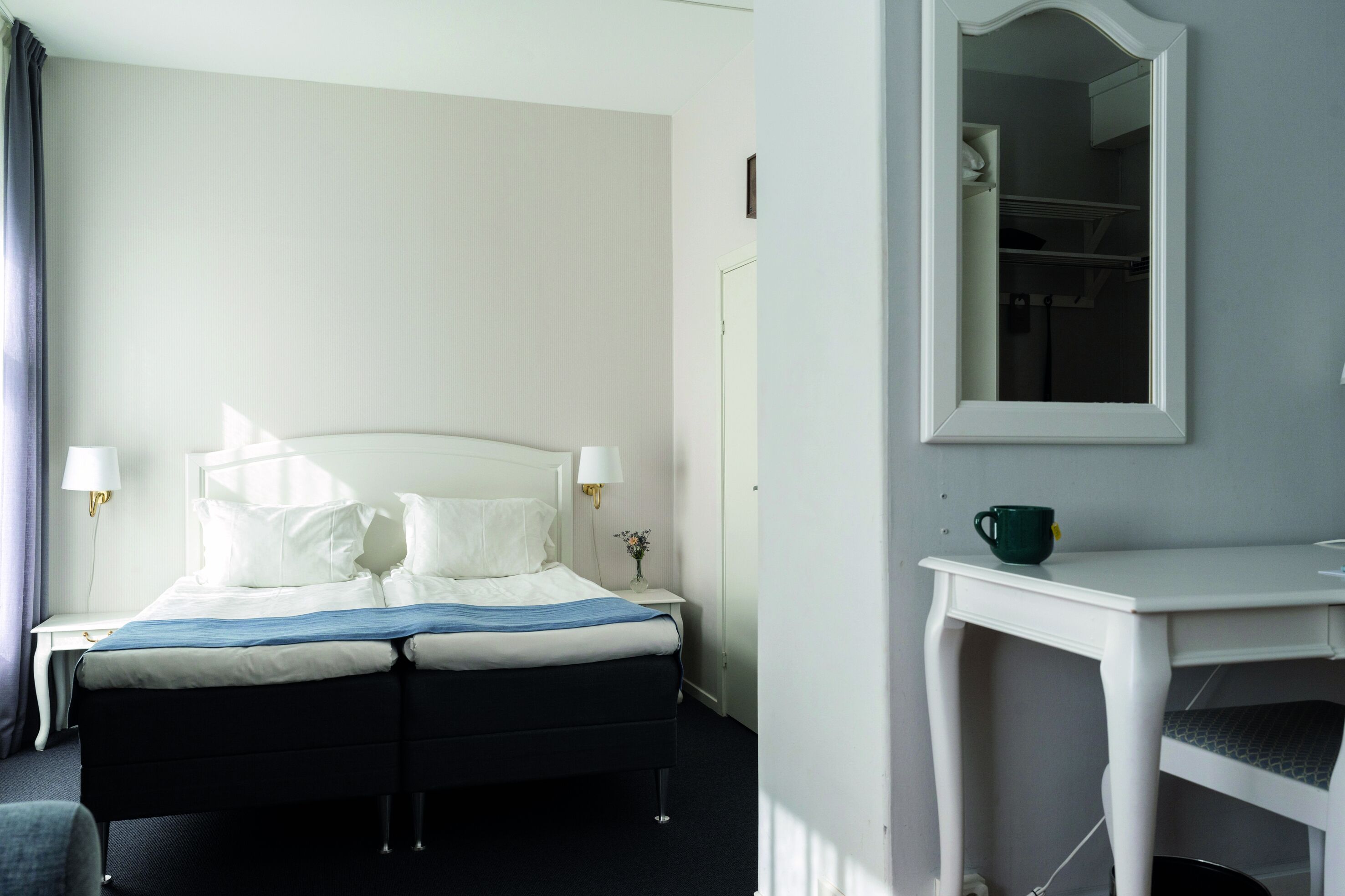 Una habitación de hotel con cama, mesita de noche, lámpara y un espejo en la pared.