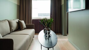 A modern living room with a sofa, a coffee table with decorative items, and a view of the outside through a window with curtains. - Elite Stadshotellet Växjö (Växjö)