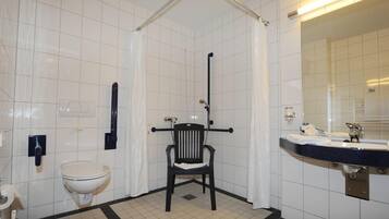 Un baño con paredes de azulejos blancos, una silla negra, un inodoro blanco y un lavabo con espejo.