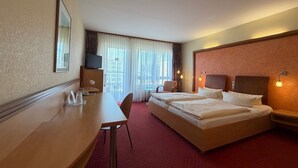 Habitación de hotel con dos camas, un escritorio, una silla, un televisor y una ventana con cortinas.