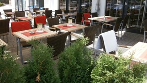 Un café al aire libre con mesas y sillas, rodeado de follaje.
