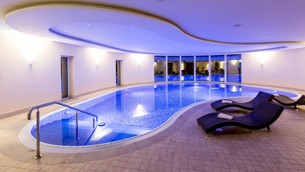 Una piscina interior moderna con diseño curvo, sillones de descanso y vistas al interior.