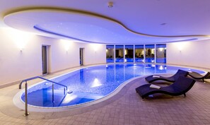 A modern indoor swimming pool with a curved design, lounge chairs, and a view of the interior. - Dorint Herrenkrug Parkhotel Magdeburg (Magdeburg)