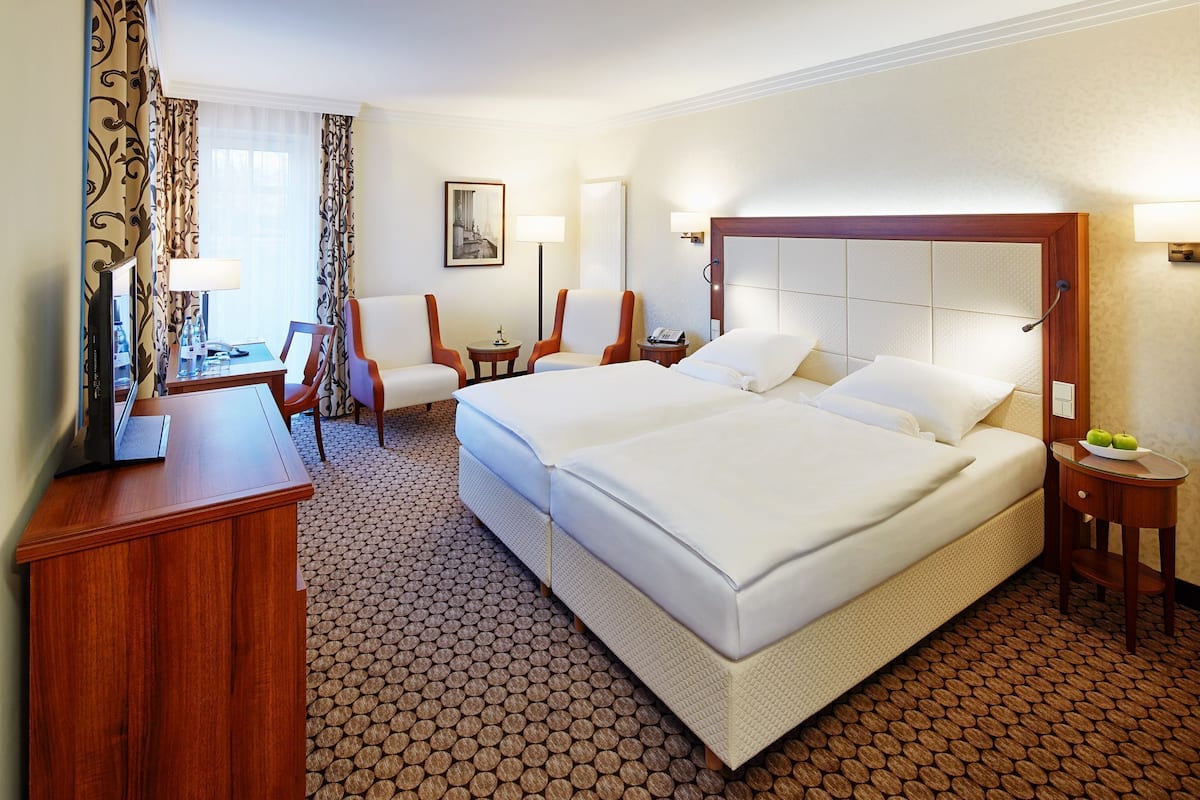 A hotel room with a large bed, two chairs, a desk with a computer, a lamp, and a small table with a phone.
