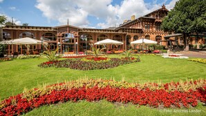 Edificio histórico con un patio que cuenta con macizos de flores rojos y amarillos, zonas de estar al aire libre y un gran árbol.