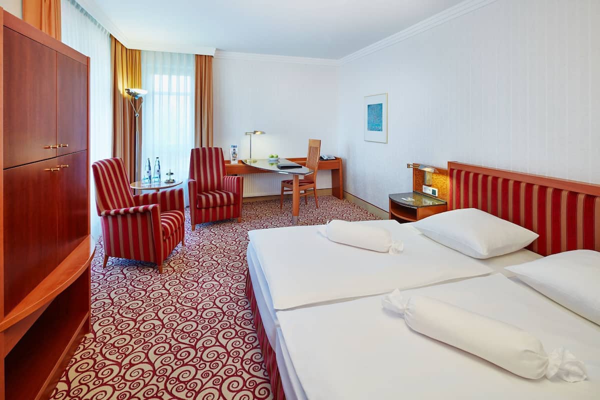 A hotel room with a large bed, two single beds, a desk with a chair, a wardrobe, and a patterned carpet.