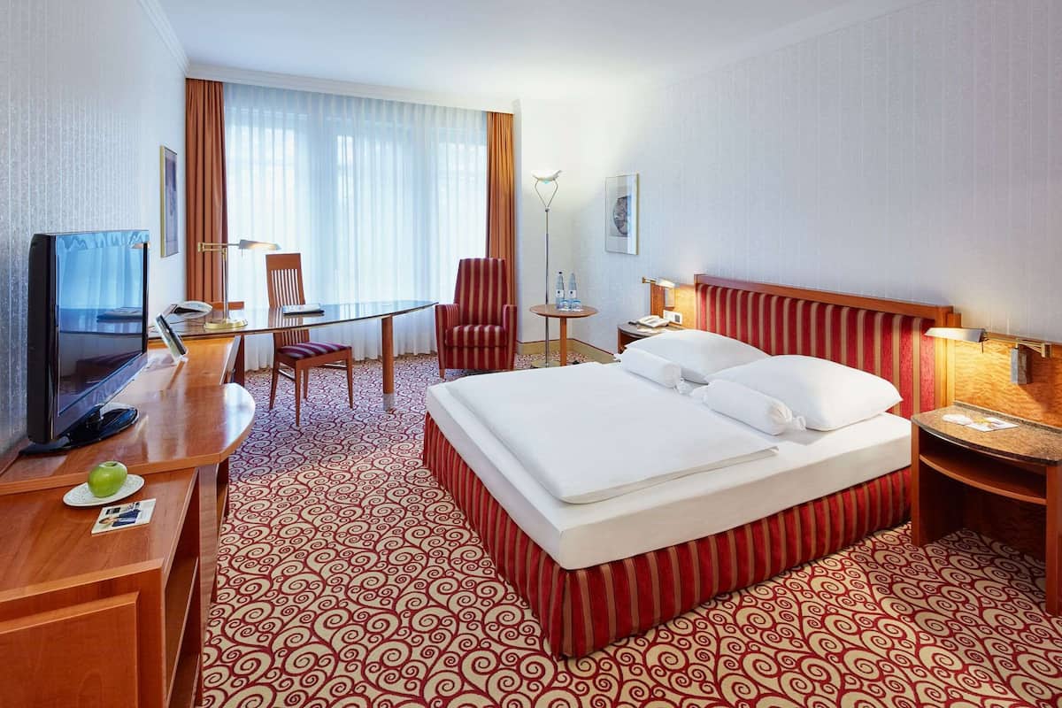 A hotel room with a bed, a desk, a chair, a television, and a lamp.