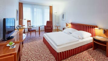 Habitación de hotel con cama, escritorio, silla, televisor y lámpara.
