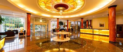 A spacious lobby with a central round table, a reception desk, and a large circular ceiling feature.