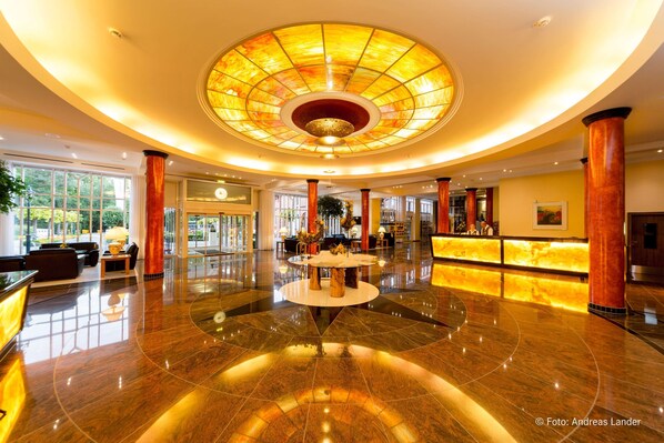 A spacious lobby with a central round table, a reception desk, and a large circular ceiling feature.