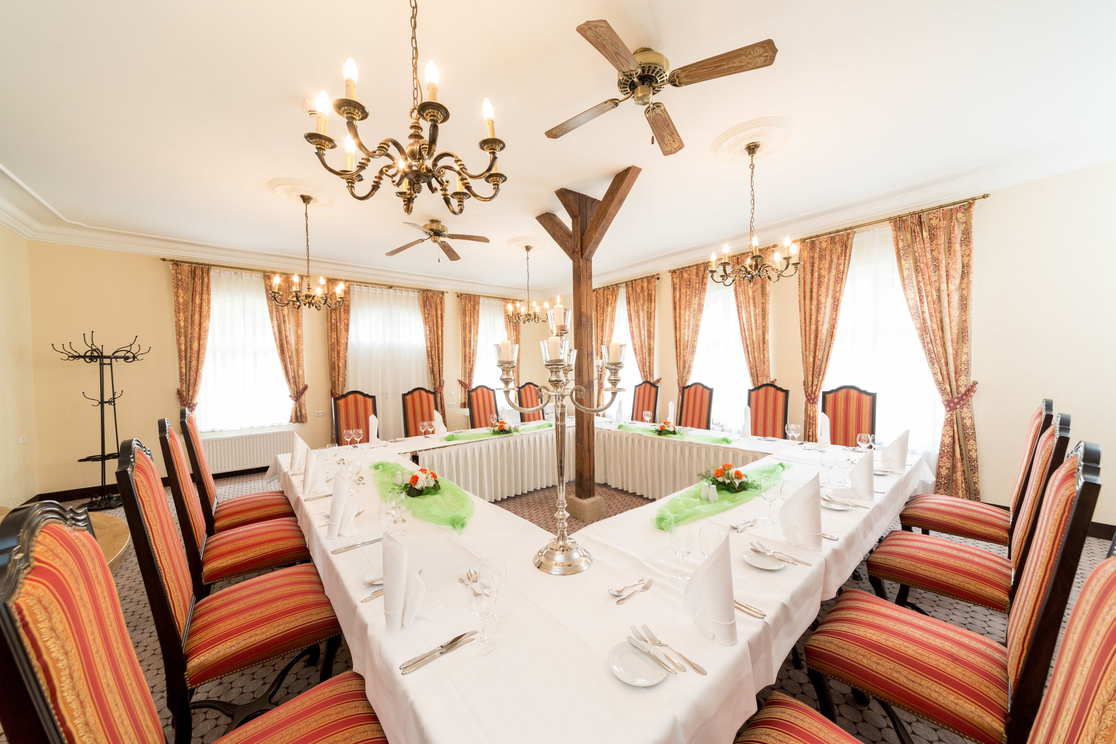 Un comedor formal con una larga mesa dispuesta para una comida, rodeada de sillas a rayas, candelabros y un ventilador de techo.