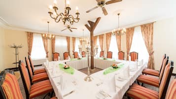 A formal dining room with a long table set for a meal, surrounded by striped chairs, chandeliers, and a ceiling fan.