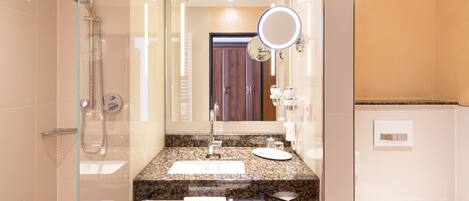 A modern bathroom with a glass-enclosed shower, a granite countertop sink, a large mirror, and a white towel rack.