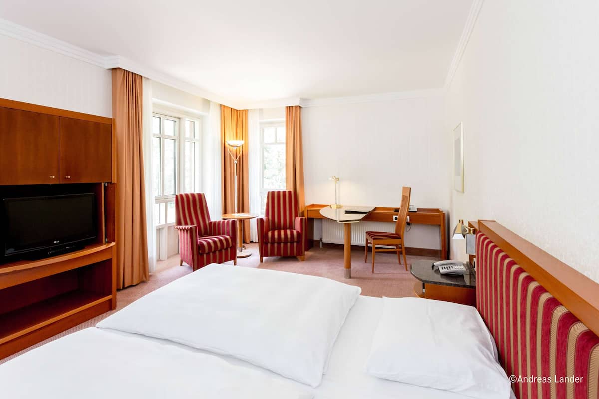 A hotel room with a bed, a TV, a desk, two chairs, and a lamp.