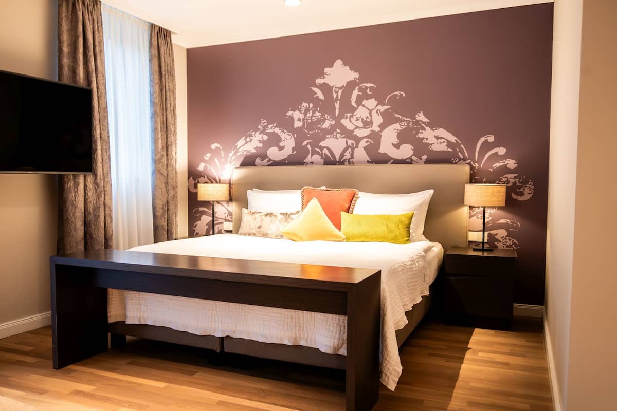 A bedroom with a bed, bedside tables, a TV, and a wall with a floral pattern.
