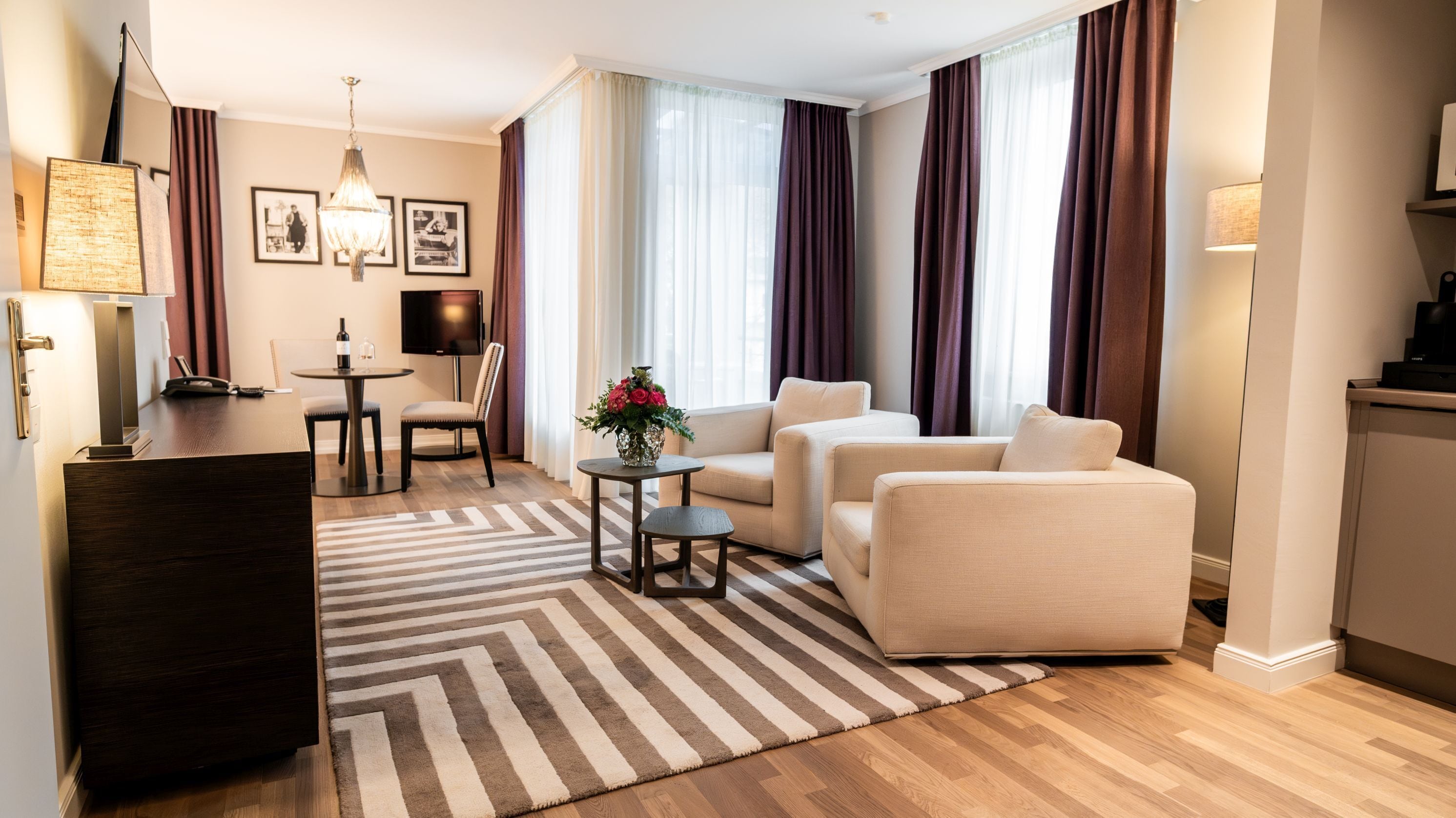 Ein modernes Hotelzimmer mit Sofa, Sessel, Esstisch und Fernseher.