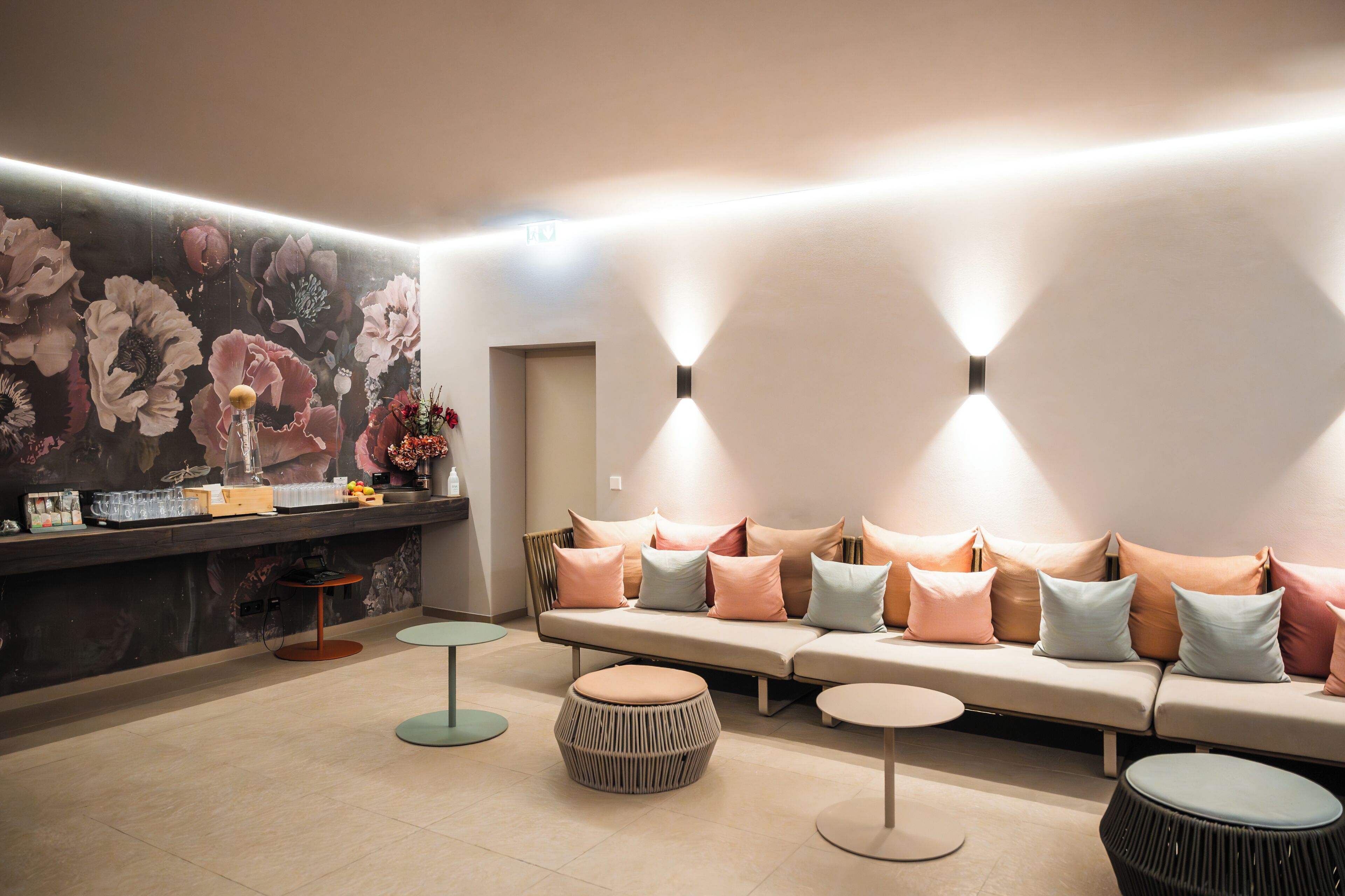 Un área de estar moderna con un sofá, otomanas redondas, una mesita y un mural floral en la pared.