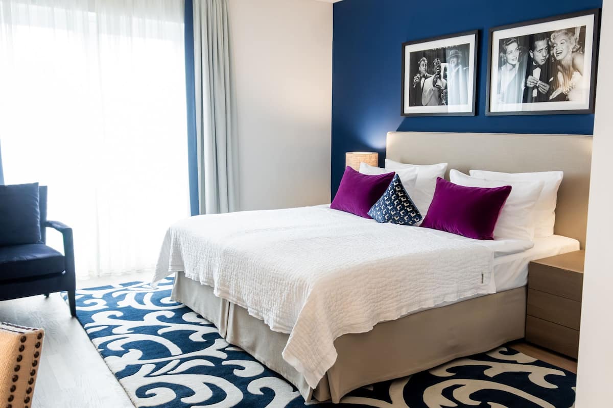 A hotel room with a bed, a chair, a desk, and a large window with curtains.