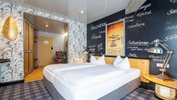 Une chambre d’hôtel avec un grand lit, un bureau avec une lampe et un mur orné de textes et de dessins.
