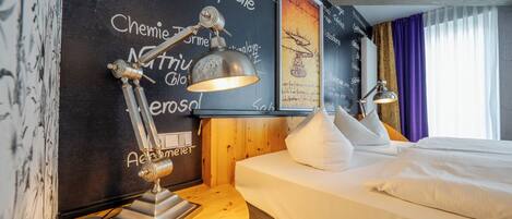 Een hotelkamer met een bed, twee bedlampen, een nachtkastje van hout, en een muur met verschillende woorden en zinnen.