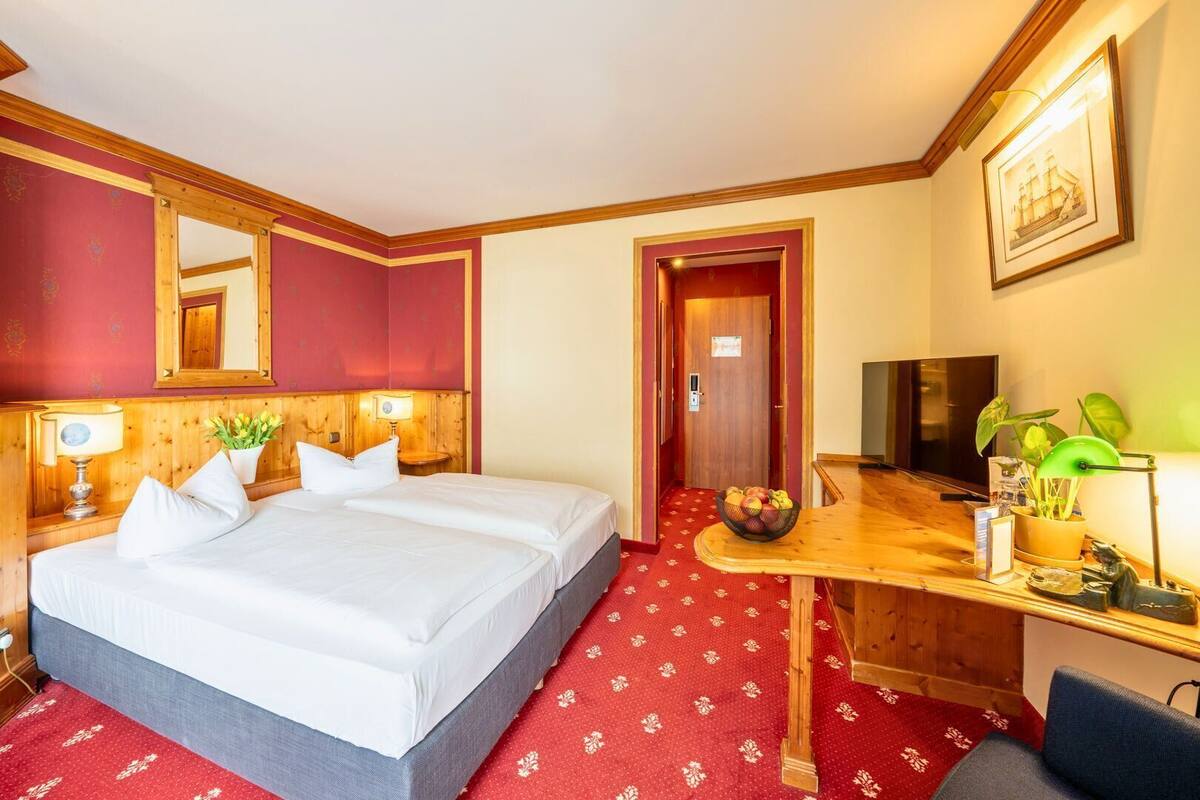 Ein Hotelzimmer mit einem großen Bett, einem Schreibtisch mit Computer, einem Fernseher und einem Spiegel.