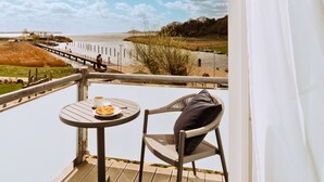 Varanda com mesa e cadeira, vista para uma praia e um cais.