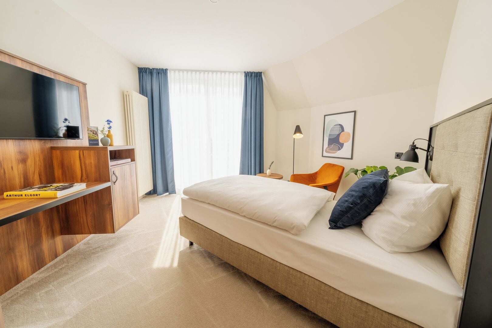 Quarto de hotel moderno com cama, escrivaninha, televisão de tela plana, cadeira e planta.