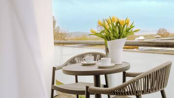 Ein runder Tisch mit zwei Stühlen, eine weiße Vase mit gelben Blumen und zwei weiße Tassen auf einem Balkon.