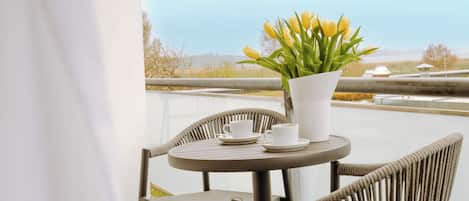 A round table with two chairs, a white vase with yellow flowers, and two white cups on a balcony.