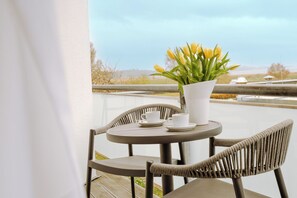 A round table with two chairs, a white vase with yellow flowers, and two white cups on a balcony. - SOLTHUS Hotel & SPA (Ostseebad Baabe)