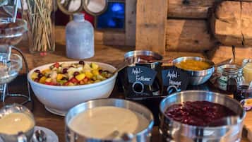 A table with various food items and beverages, including a bowl of fruit salad, a bowl of soup, and several containers of condiments.