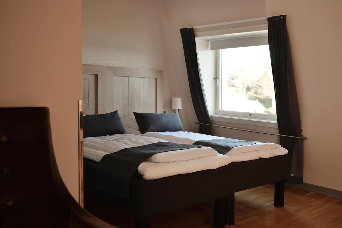 A bed with a wooden headboard, a window with curtains, and a lamp on the nightstand.
