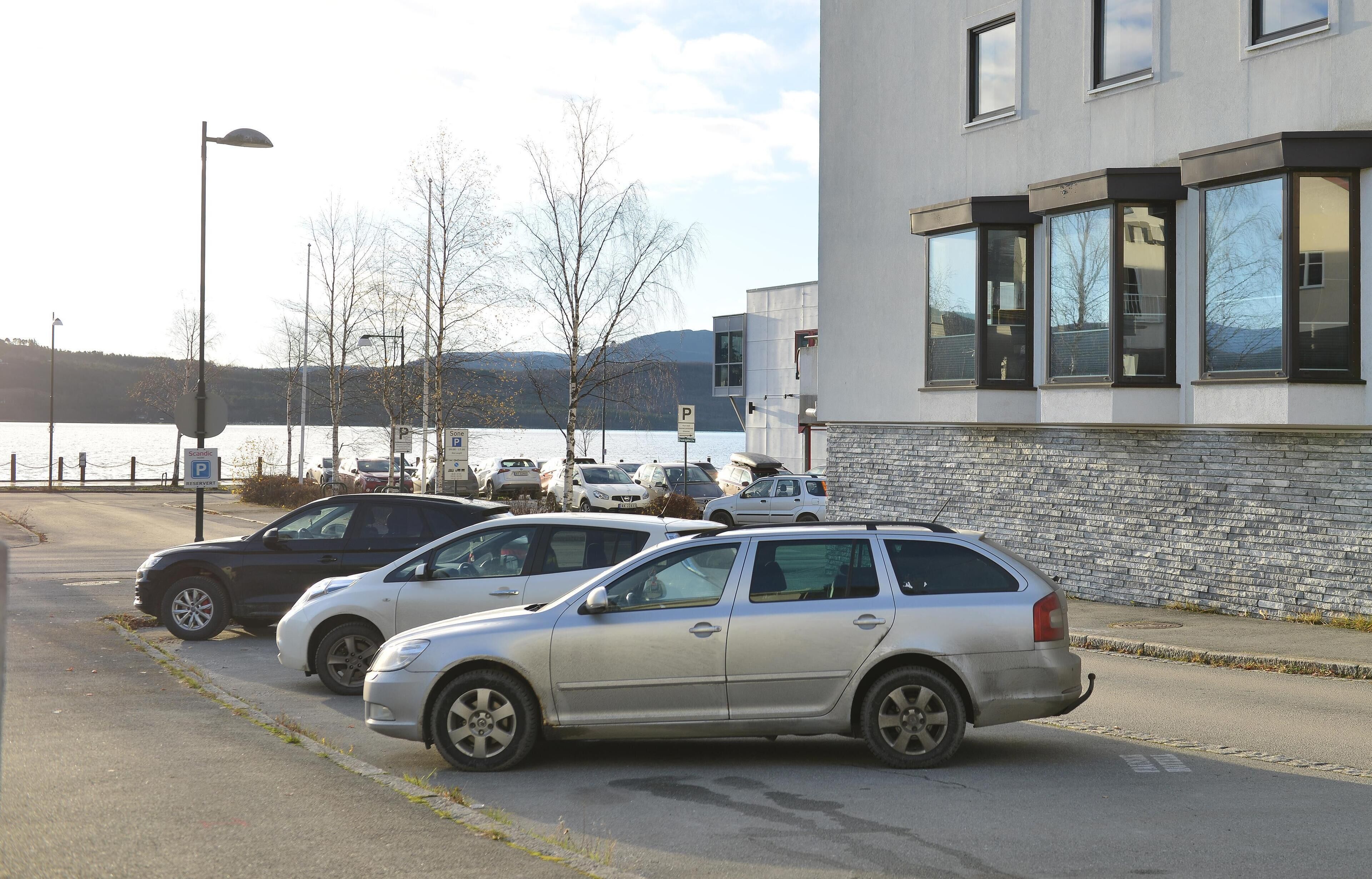 A parking area with cars parked in front of a building with large windows and a stone facade.