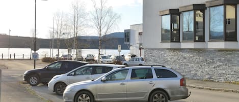 Un estacionamiento con autos estacionados frente a un edificio de grandes ventanales y fachada de piedra.