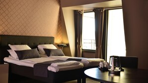 A neatly made bed with pillows and a blanket, a bedside table with a lamp, and a view of the outdoors through a window with curtains. - Scandic Fauske Hotel (Fauske)