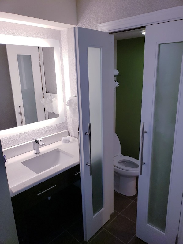 A bathroom with a white sink, a mirror, and a toilet. - Baymont by Wyndham Slidell (Slidell)