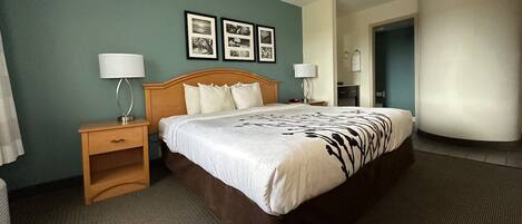 A hotel room with a large bed, two bedside tables with lamps, a wooden nightstand, and a wall with framed pictures.