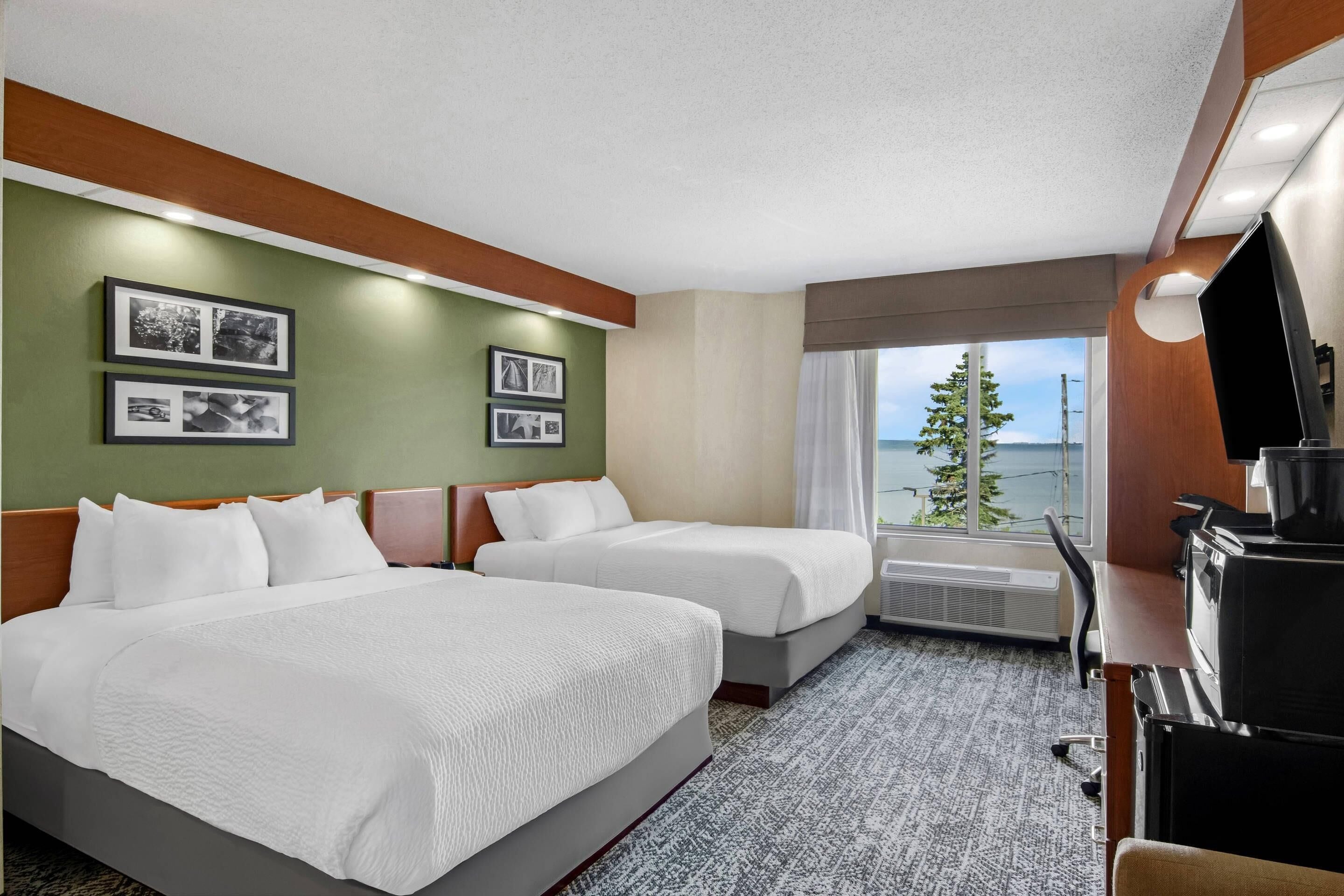 A hotel room with two beds, a desk with a TV, and a window with a view of the ocean.