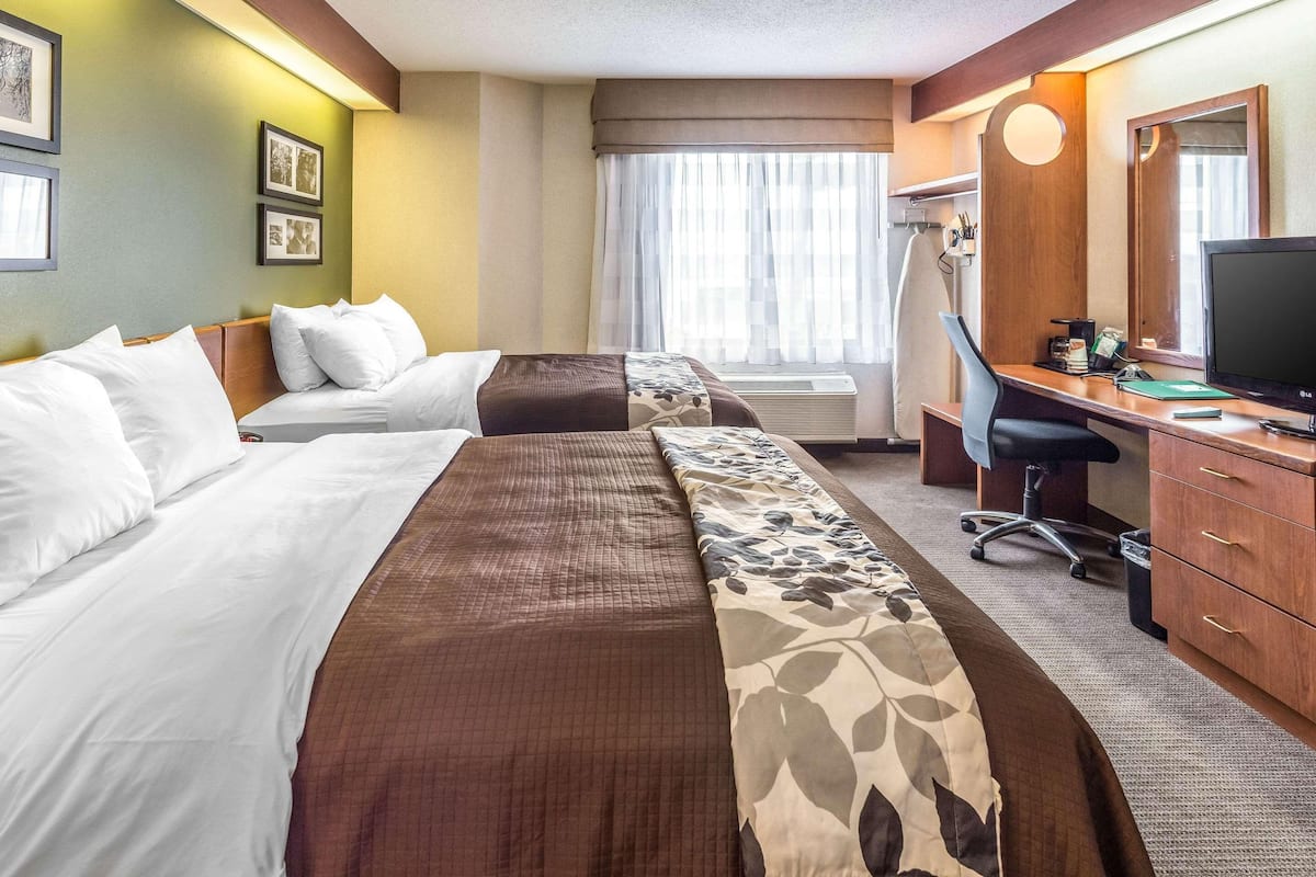 A hotel room with two beds, a desk with a computer, a chair, a mirror, and a window with curtains.